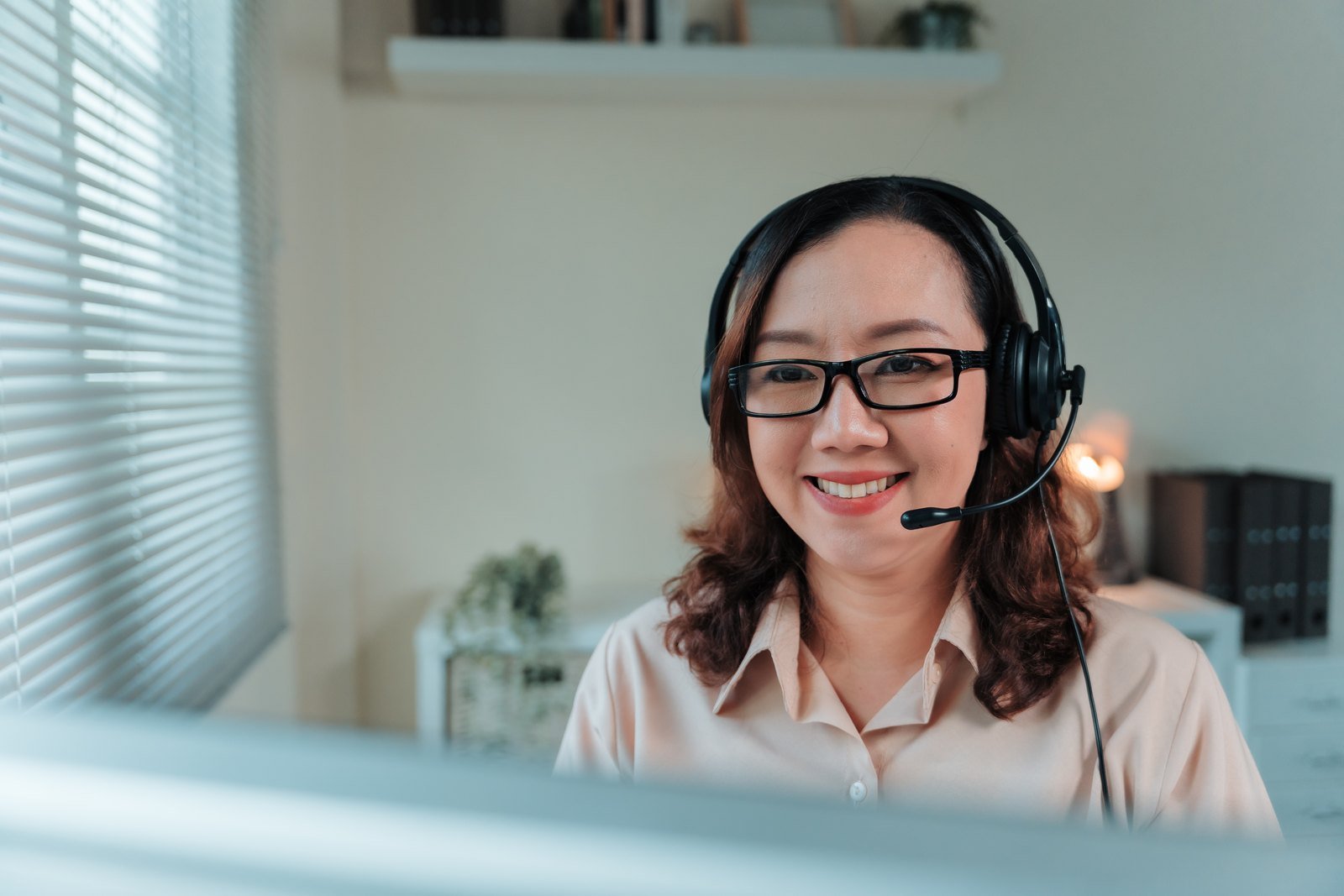 Customer support professional smiling at her workstation while wearing a headset