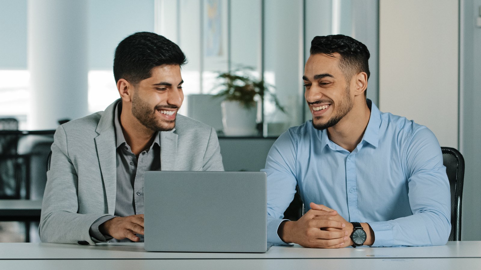 Coworkers discussing work around laptops in a bright office