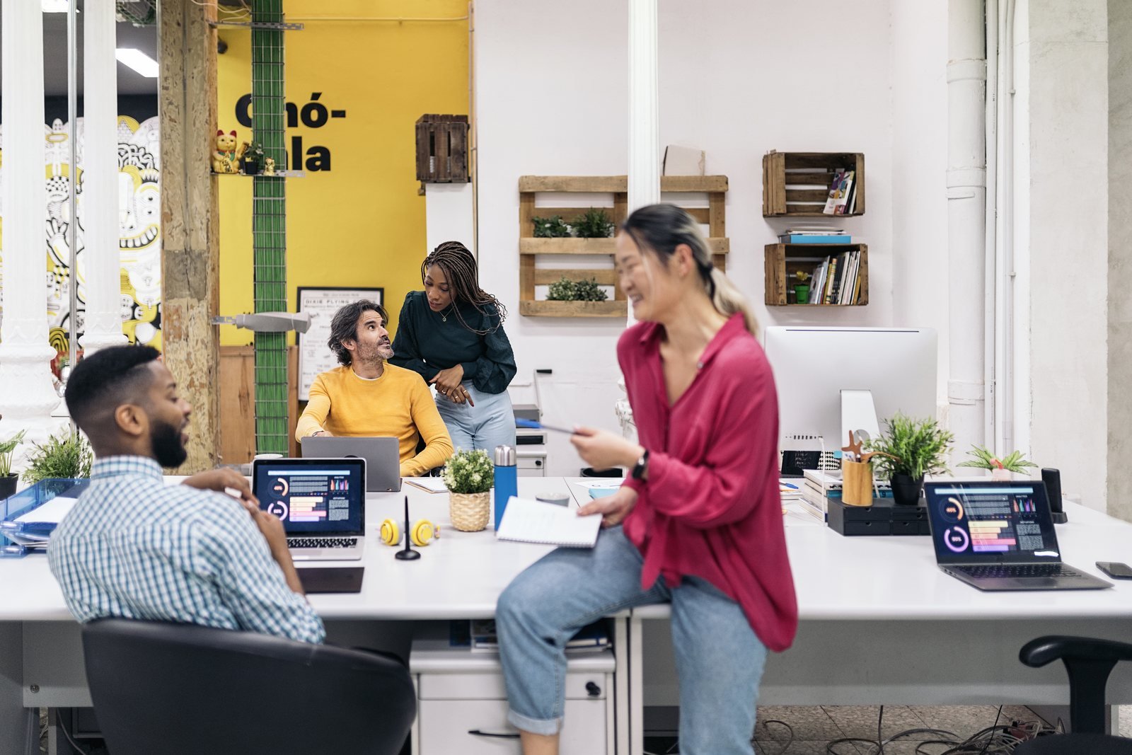 Coworkers smiling and collaborating around laptops in a bright office